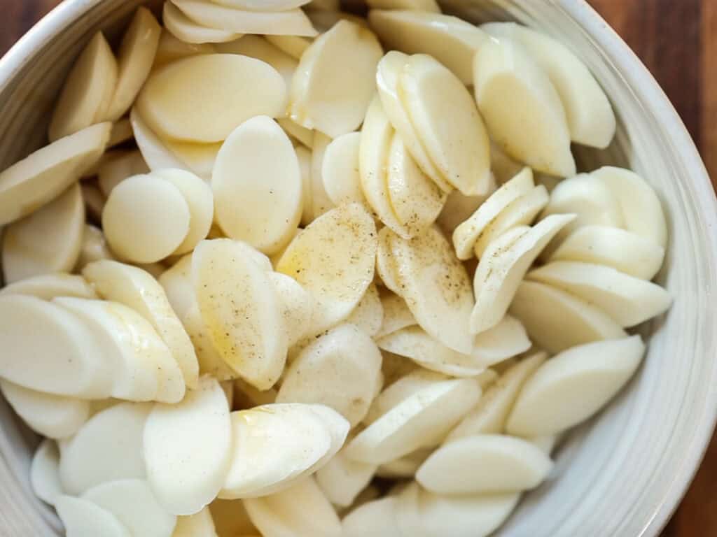 A bowl filled with thinly sliced rice cakes, lightly seasoned with pepper, on a wooden surface.